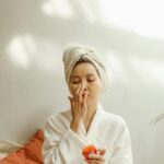 Asian woman in a robe applying skincare cream. Relaxing indoor beauty routine.