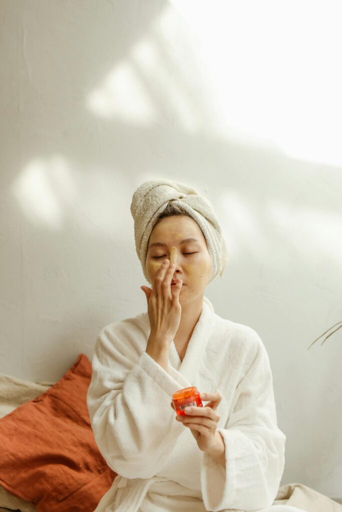 Asian woman in a robe applying skincare cream. Relaxing indoor beauty routine.